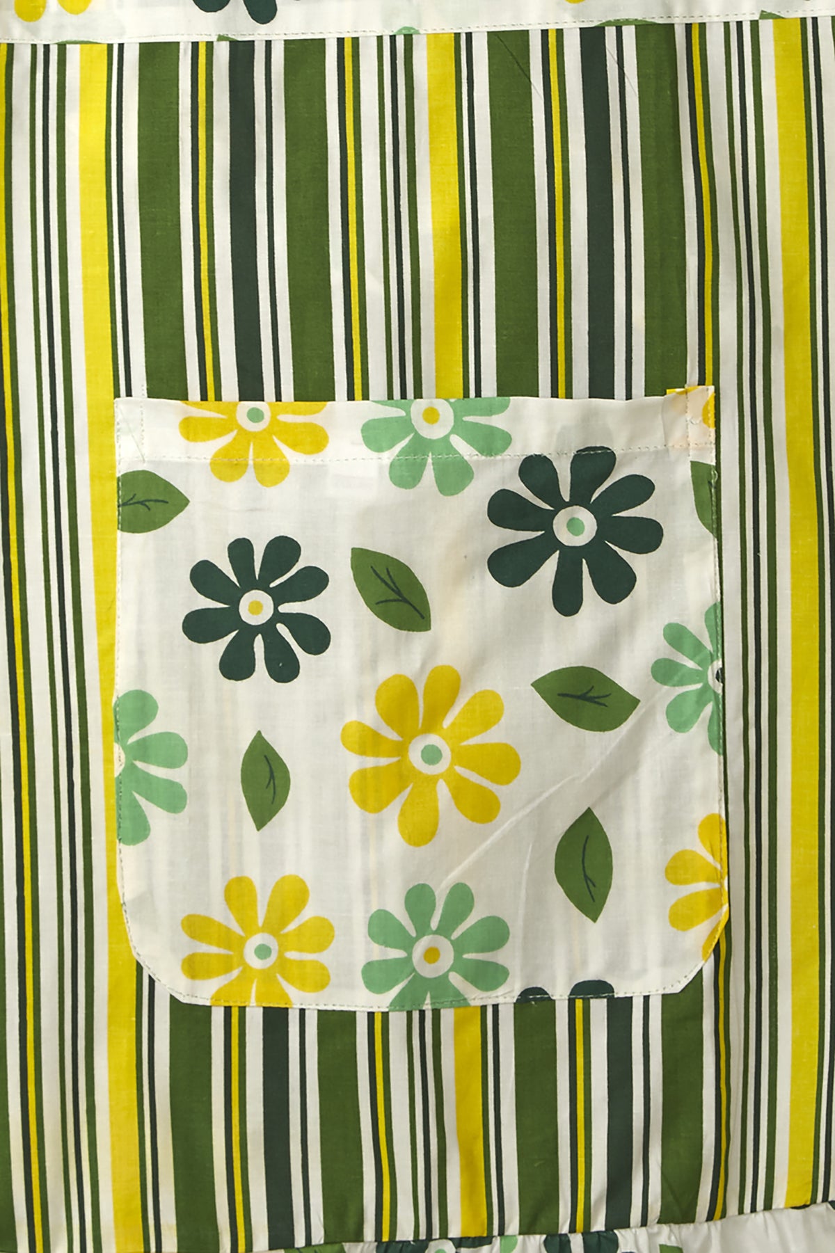 Close-up of the dark yellow bohemian print, roomy pocket and frilly hem on an In-Sattva cotton apron