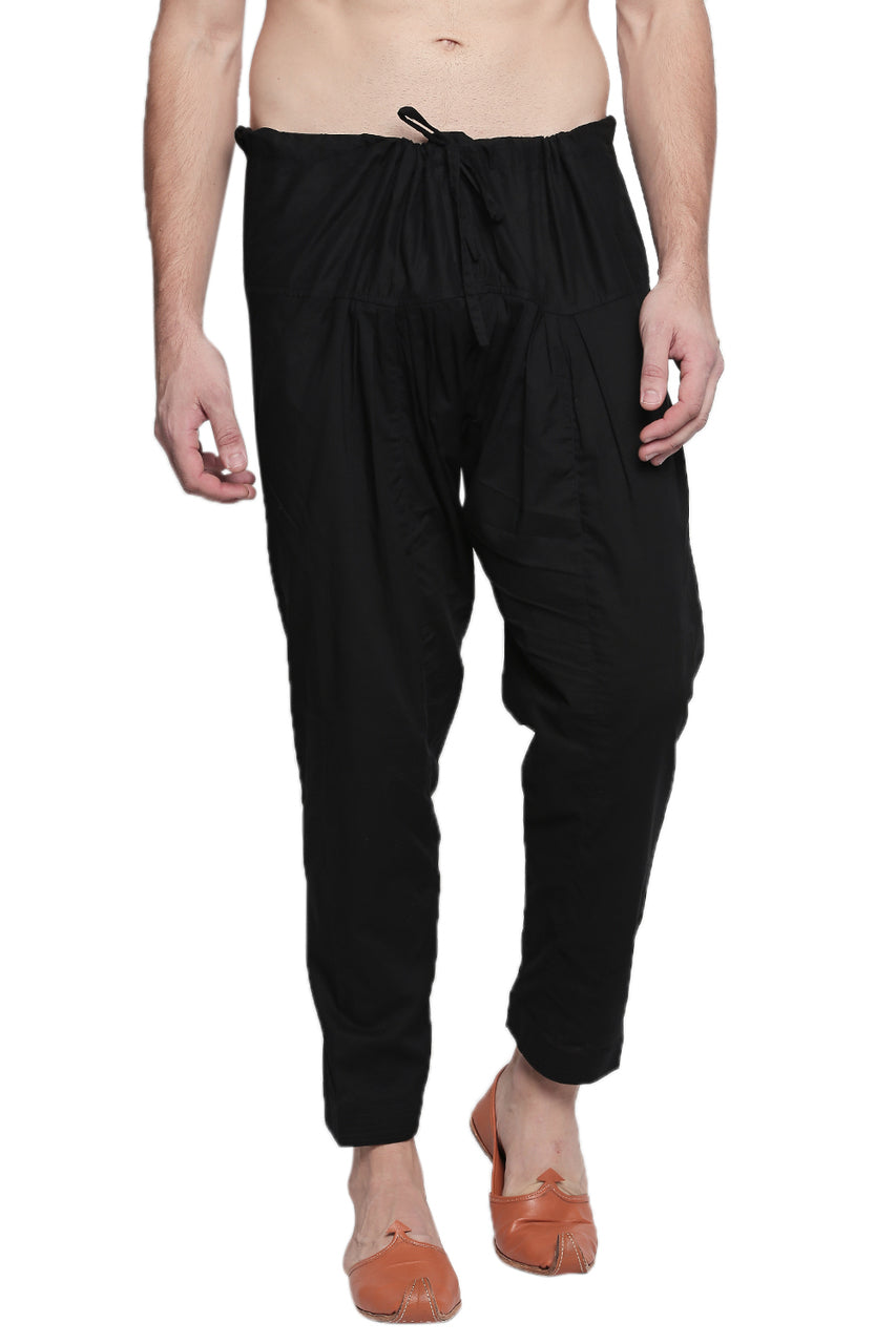Front view of In-Sattva men's black cotton baggy salwar yoga pants, showing the drawstring waistband, roomy hips and tapered ankles.
