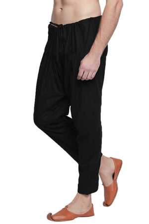 Left profile view of In-Sattva men's black cotton baggy salwar yoga pants, showing the baggy hip shape narrowing into the tapered ankle.
