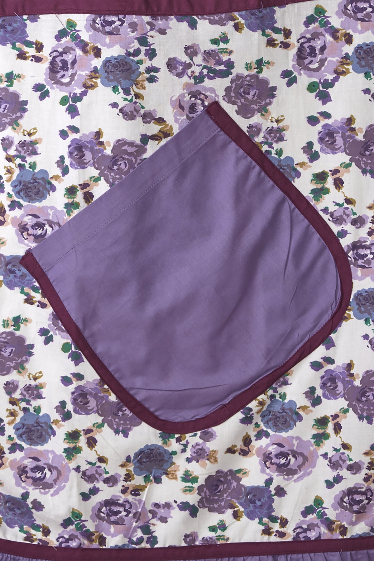 Close-up of the purple bohemian print, roomy pocket and frilly hem on an In-Sattva cotton apron