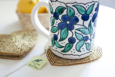 Close-up of a floral coffee mug on a Rangeene gold glass beaded heart shaped coaster