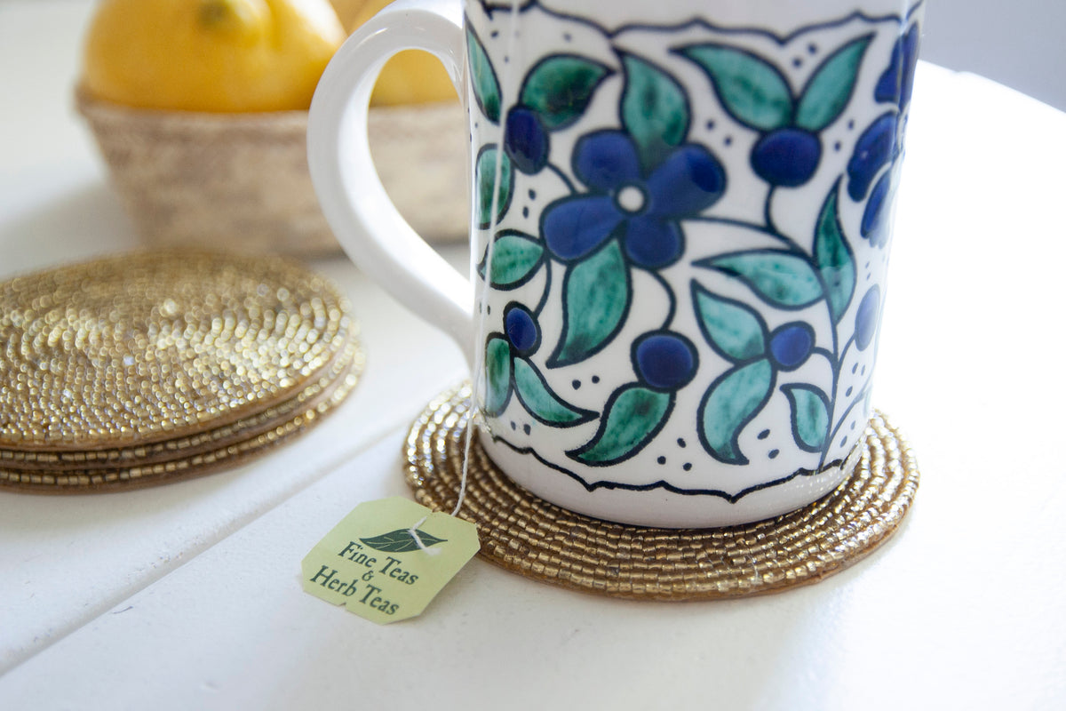 Close-up of a floral coffee mug on a Rangeene gold glass beaded round coaster