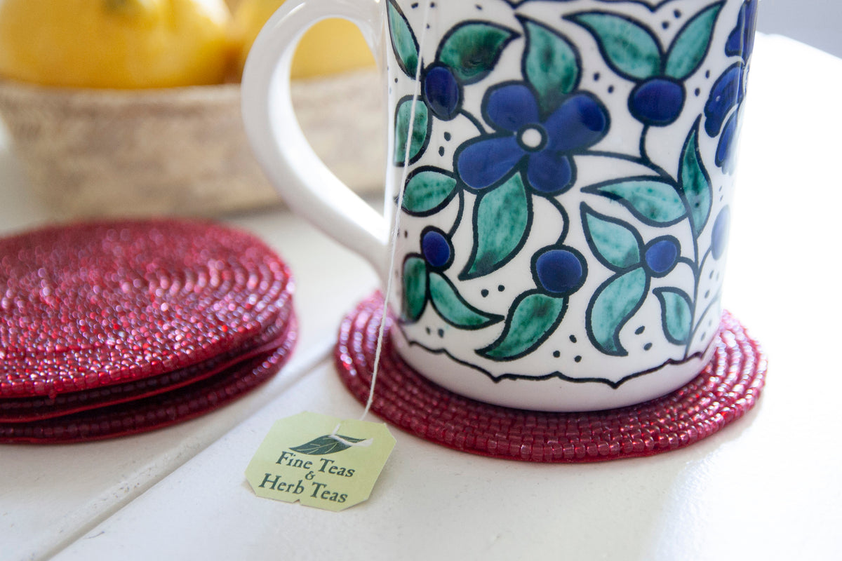 Close-up of a floral coffee mug on a Rangeene red glass beaded round coaster
