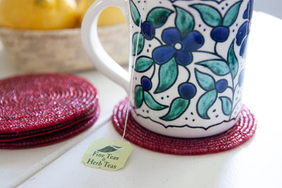 Close-up of a floral coffee mug on a Rangeene red glass beaded round coaster
