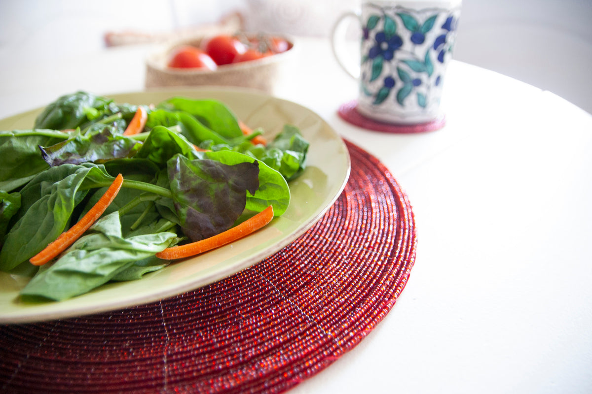 Close-up of red glass beadwork beneath a salad plate on a Rangeene round placemat