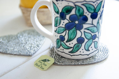 Close-up of a floral coffee mug on a Rangeene silver glass beaded heart shaped coaster