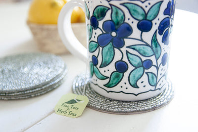 Close-up of a floral coffee mug on a Rangeene silver glass beaded round coaster