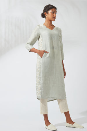 Styled front view of Jove women's gray silk-linen kurta shift dress, featuring white floral embroidery along the side panel, three-quarter sleeves and a relaxed fit, with the model standing with one hand on her hip.