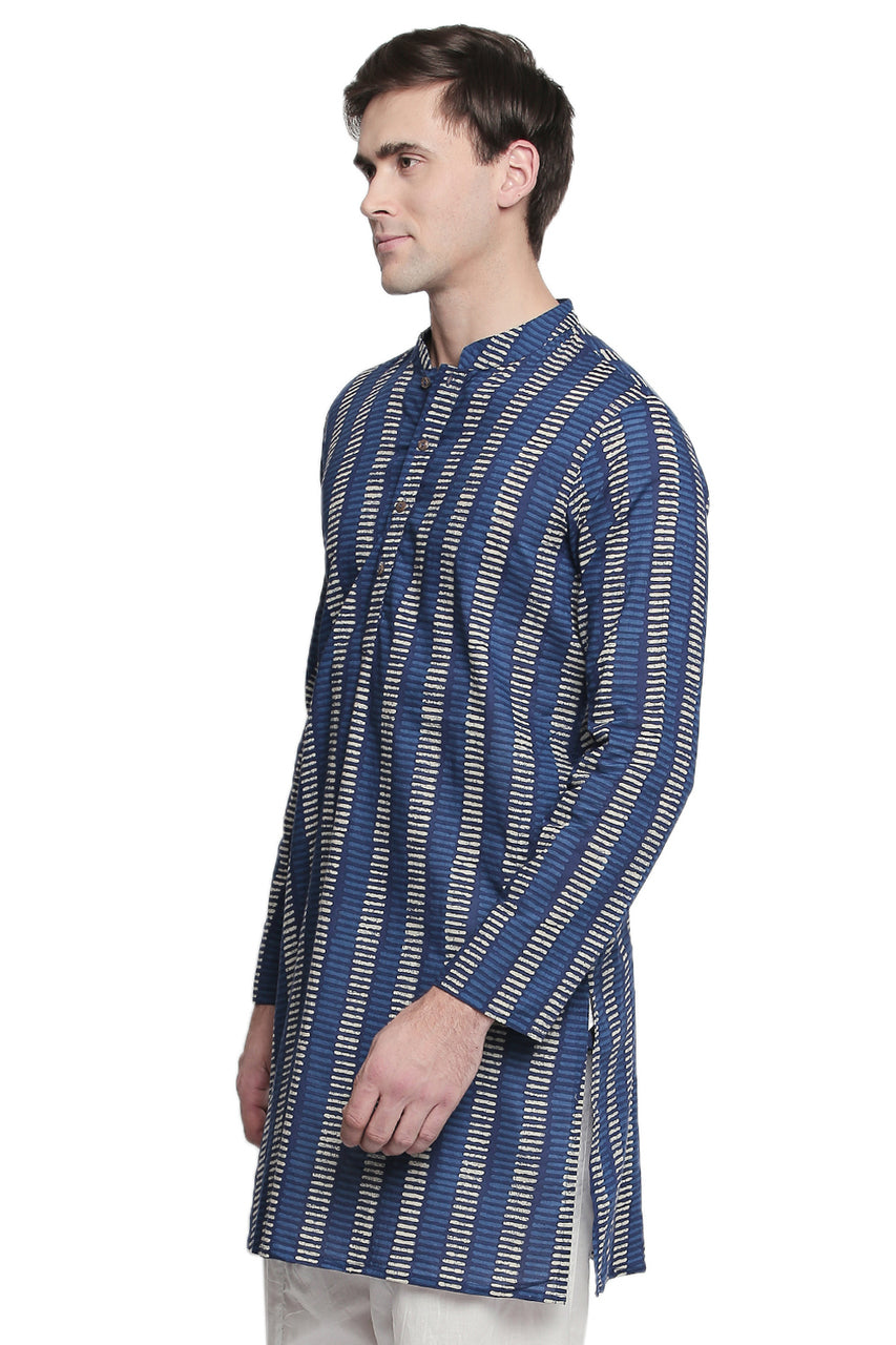 Side view of a model wearing In-Sattva's men's indigo block print cotton thigh-length kurta tunic, featuring a band collar, long sleeves, button placket and cream-colored block print pattern. The side slit is visible.